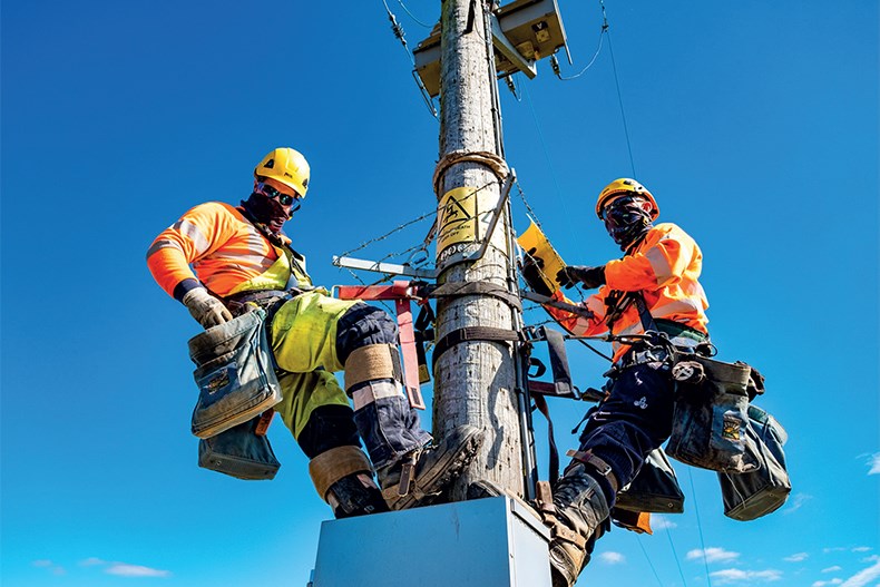 Two electrical engineers climbing a electricity pole in high visibility PPE